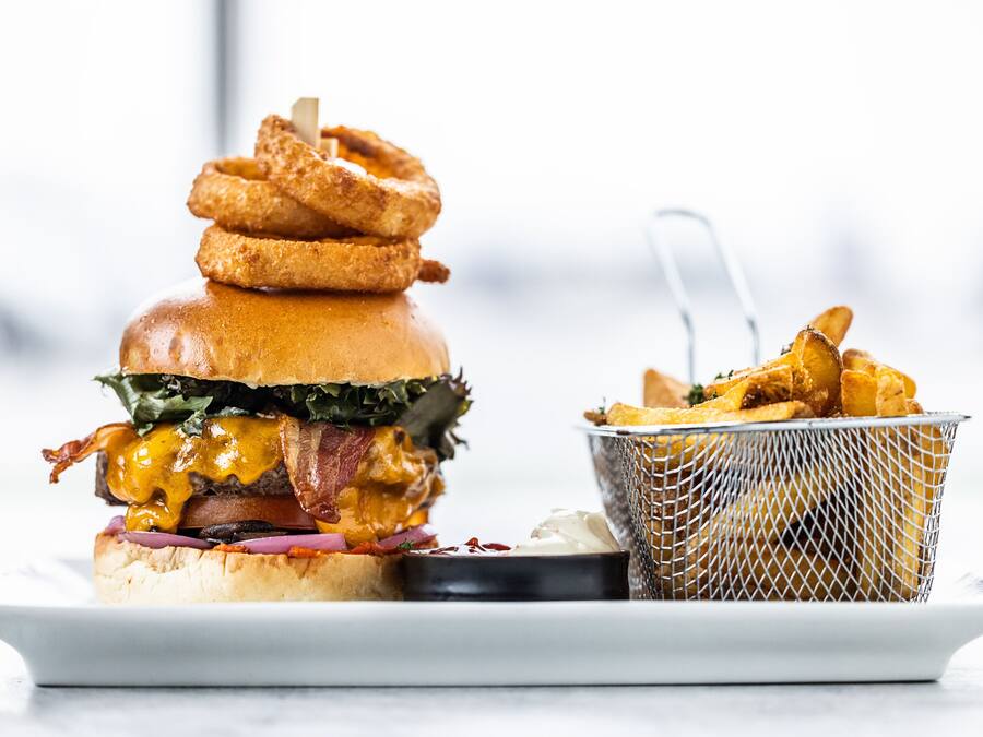 Una hamburguesa con tocino, queso y lechuga, acompañada de aros de cebolla y una porción de papas fritas.