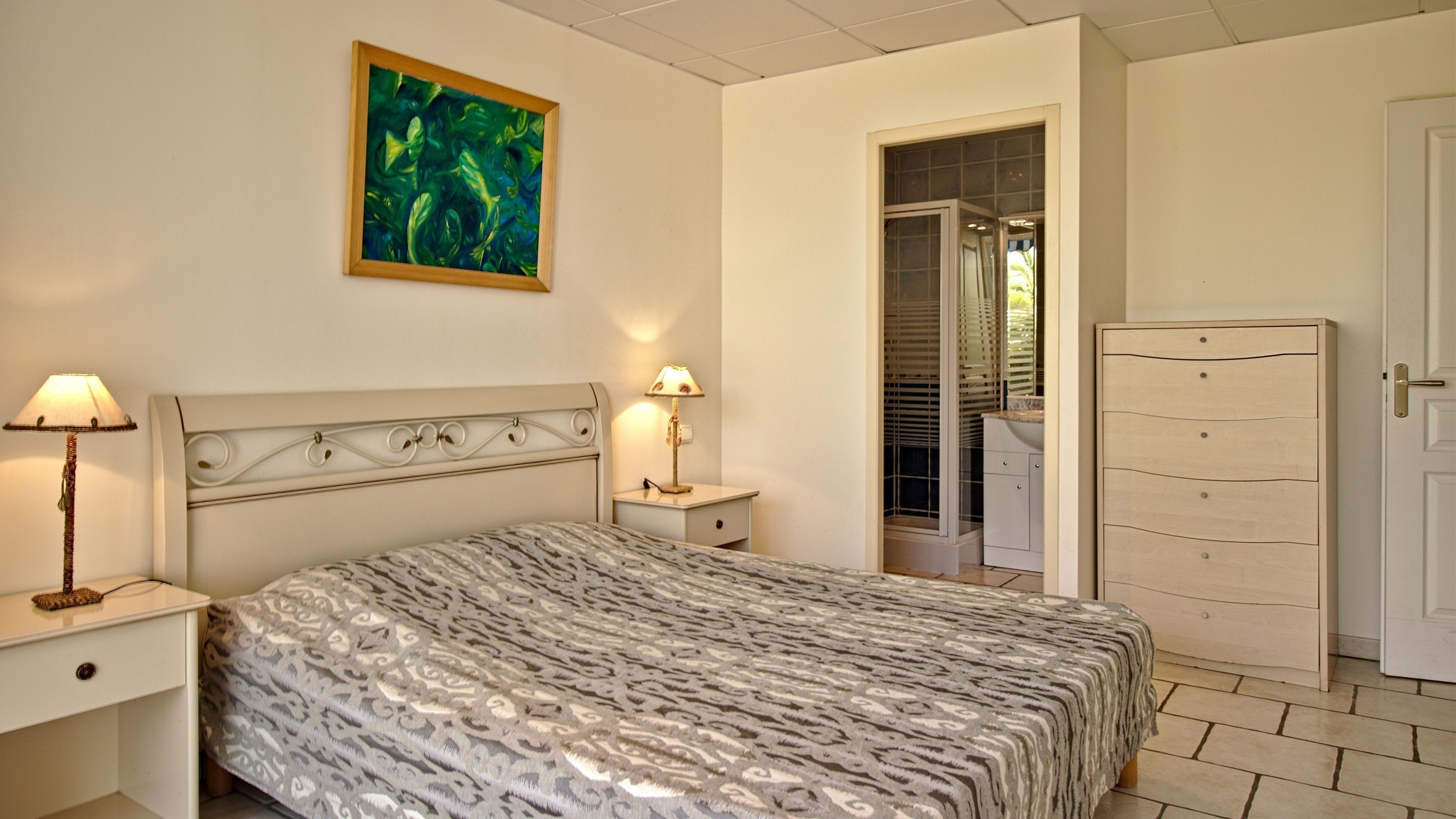 Ein Schlafzimmer mit einem gemusterten Bett, zwei Nachttischlampen, einem Nachttisch, einem Kleiderschrank und einem Bild an der Wand.