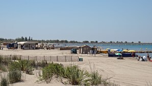 Zona de playa con bar y restaurante, una pequeña cabaña de madera y sombrillas.