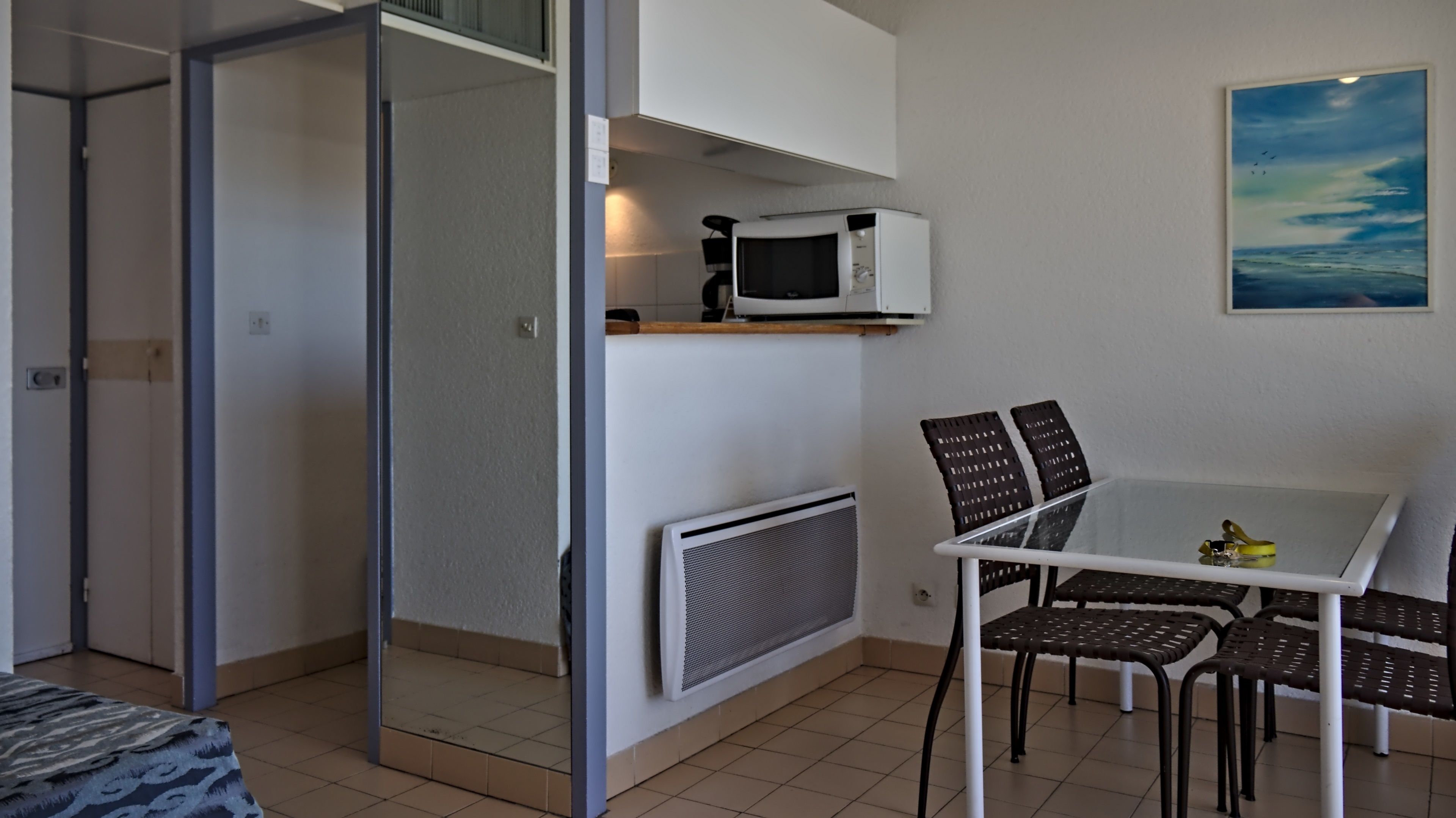 Et kompakt værelse med skydedør til balkon, et lille bord med stole, mikroovn og radiator.