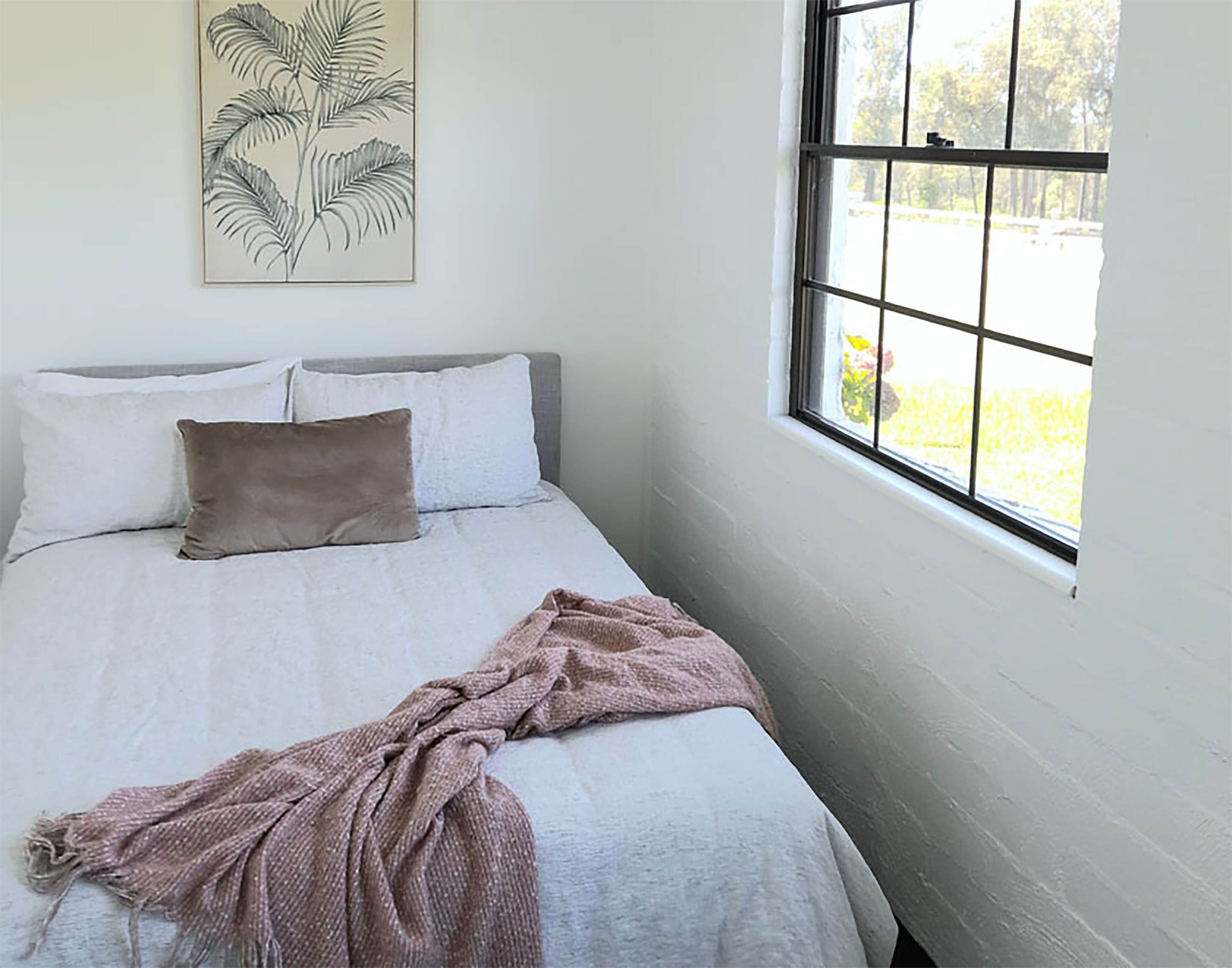 A bedroom with a bed, pillows, a blanket, a window, and a wall art piece.