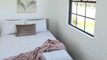A bedroom with a bed, pillows, a blanket, a window, and a wall art piece.