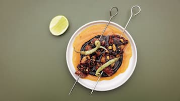 A plate of skewered octopus with a lime wedge on a green background.