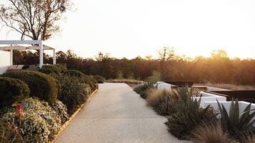 A pathway leading to a white gazebo with a bench, surrounded by neatly trimmed hedges and various plants.