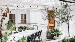 An outdoor dining area with a long table and chairs, surrounded by potted plants and a pergola with string lights. - The Oaks Ranch (Mossy Point)