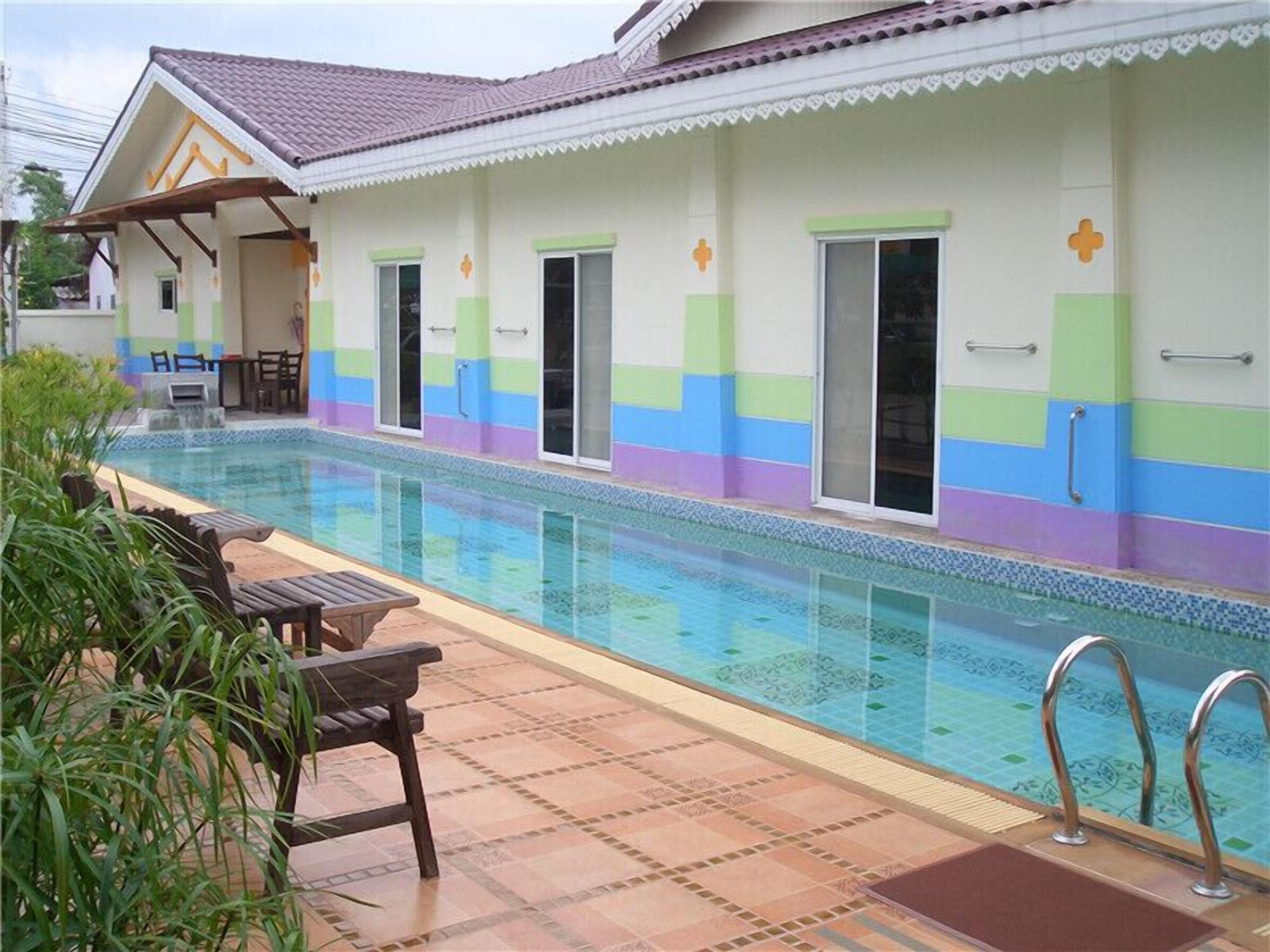 A swimming pool with a tiled deck, a covered seating area, and a building with colorful walls and doors.
