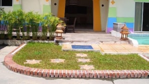 A building with a covered entrance, a small pool area, and a garden with plants and a brick border. - Phuket7-inn Hotel (Chalong)