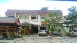 A two-story building with a car parked in front. There is a spiral driveway leading to the entrance. - Phuket7-inn Hotel (Chalong)
