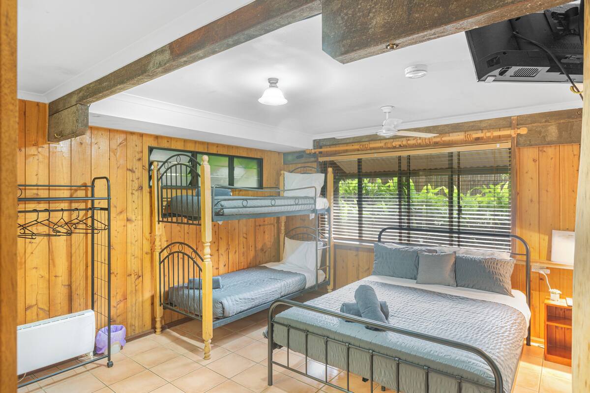 Une cabane en bois avec des lits superposés, un lit simple et une fenêtre avec des stores.