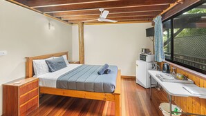 Een slaapkamer met een houten bed, een bureau, een magnetron en een raam met uitzicht op groen.
