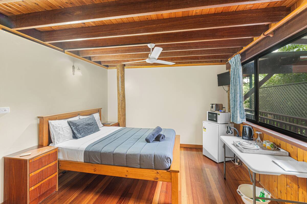 Une chambre avec un lit en bois, un bureau, un four à micro-ondes et une fenêtre donnant sur un paysage verdoyant.