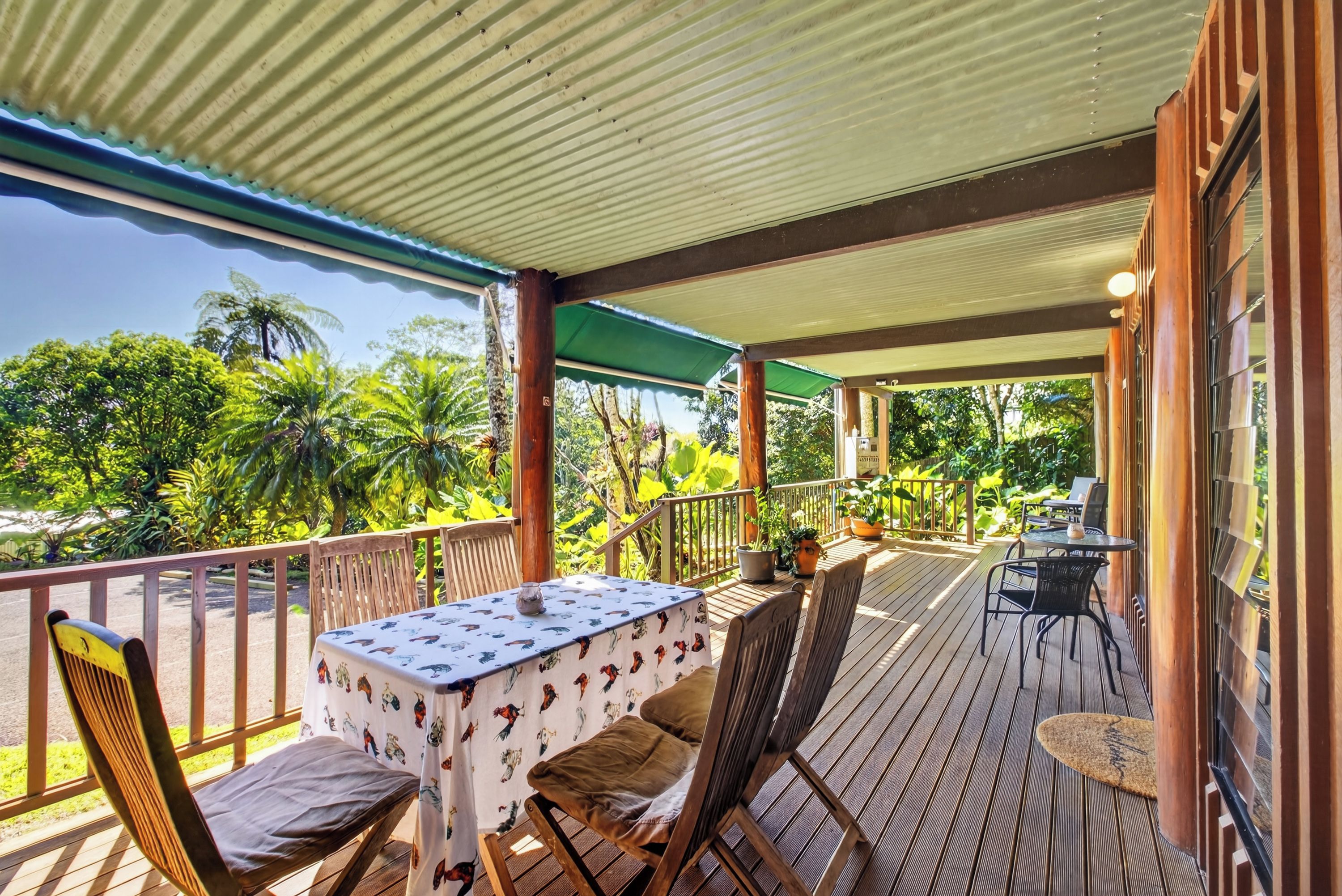 A covered outdoor seating area with a table and chairs, surrounded by lush greenery and a view of the landscape.