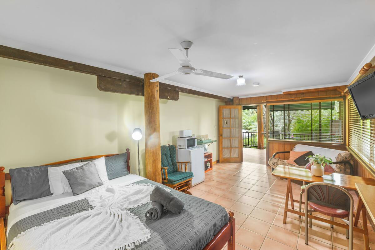 Une chambre à coucher comprenant un lit, un bureau, une chaise, un téléviseur et un balcon avec vue sur la verdure.