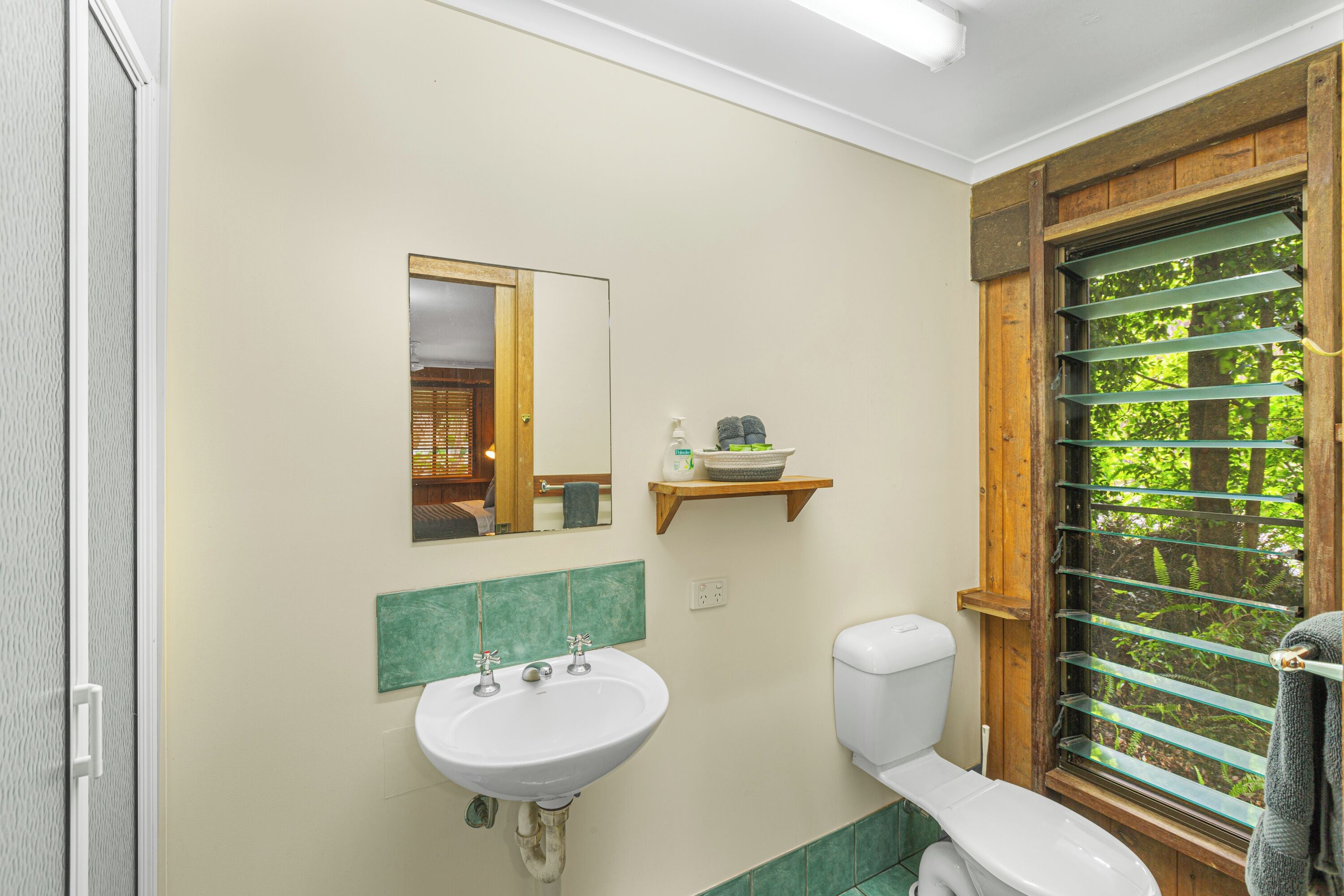 A bathroom with a sink, toilet, and a window with a view of greenery.