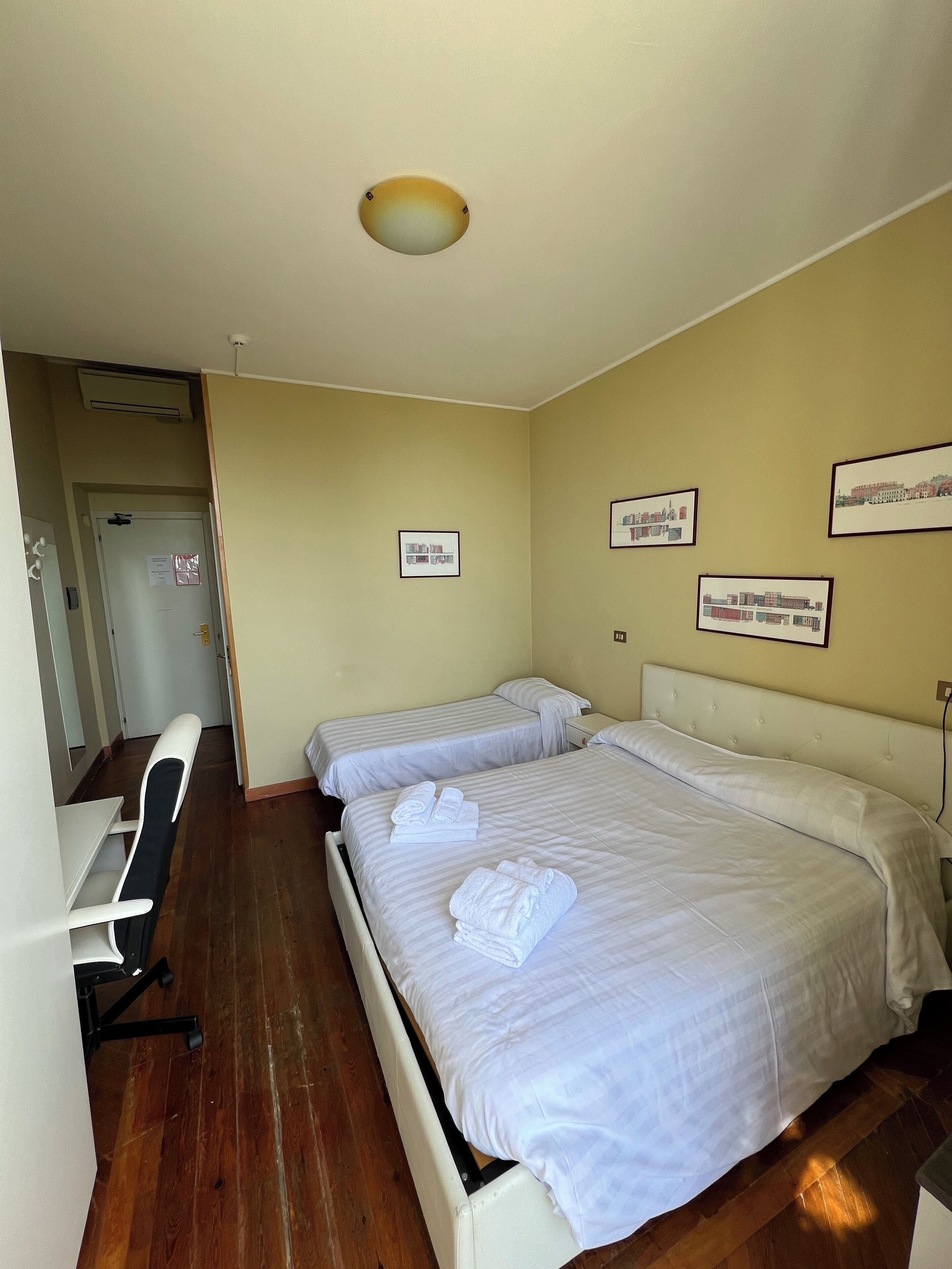 Habitación de hotel con dos camas, un escritorio y una silla. Hay cuadros en la pared.