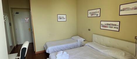 A hotel room with two beds, a desk, and a chair. There are framed pictures on the wall.