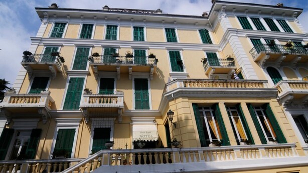 A multi-story hotel with balconies, green shutters, and a classic architectural style. - Hotel Petit Royal (Ospedaletti)