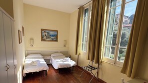 A hotel room with two beds, a painting on the wall, a window with curtains, and a wooden floor. - Hotel Petit Royal (Ospedaletti)