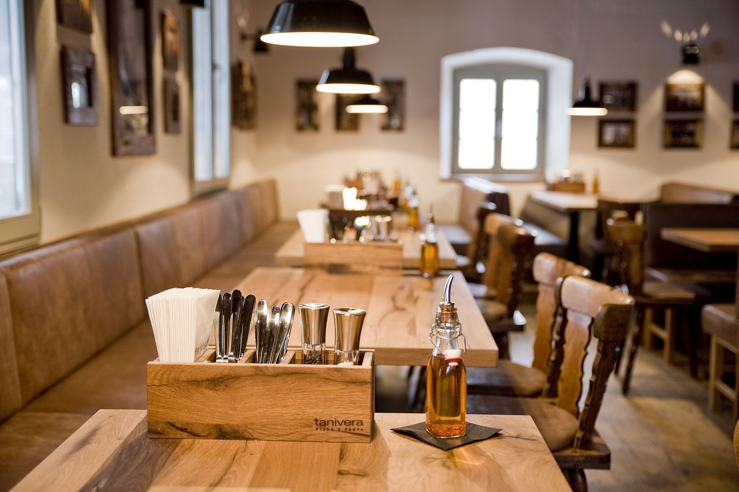 A restaurant interior with wooden tables, benches, and a variety of cutlery in a holder.