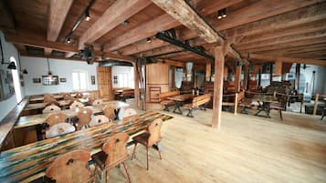 Un comedor amplio con mesas y sillas de madera, vigas a la vista y una decoración rústica.