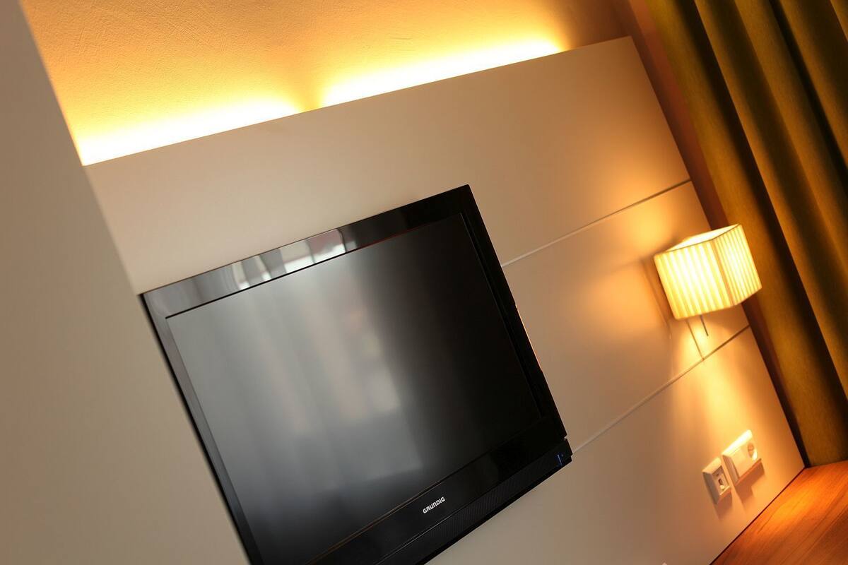 A modern wall-mounted flat-screen TV in a hotel room with a wall-mounted lamp and a power outlet.
