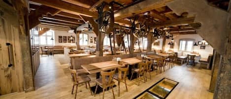 A rustic wooden interior with exposed beams, wooden tables and chairs, and a central area with a glass floor.