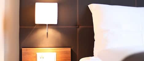 A neatly made bed with a dark headboard and a bedside table with a lamp.