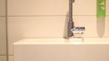 Un baño con un lavabo blanco, un espejo y dos toallas colgadas en un perchero.