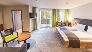 A hotel room with a bed, a desk, a chair, a TV, and a view of the outdoors. - Hotel Kunstmühle (Mindelheim)