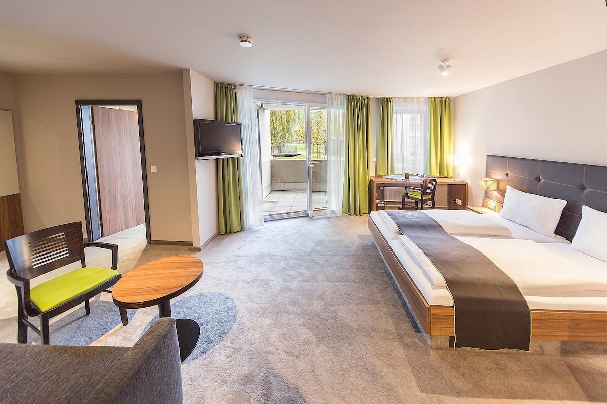 A hotel room with a bed, a desk, a chair, a TV, and a view of the outdoors.