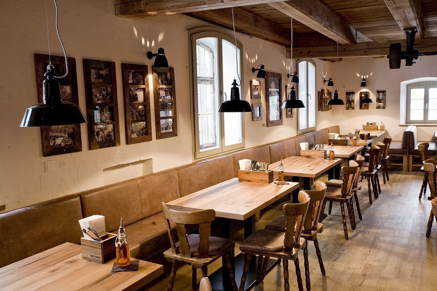 Un restaurante con mesas y bancos de madera, luces colgantes y cuadros en las paredes.
