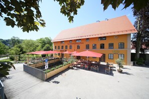 A building with a red-tiled roof and a yellow facade, featuring outdoor seating with red umbrellas and a garden area. - Hotel Kunstmühle (Mindelheim)
