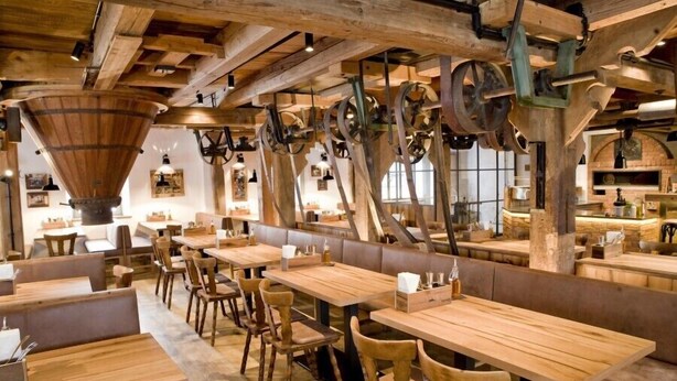 A rustic restaurant interior with wooden tables and benches, exposed beams, and vintage industrial elements like pulleys and a large funnel. - Hotel Kunstmühle (Mindelheim)