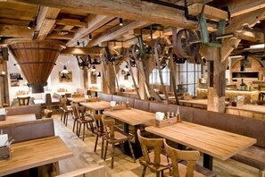 Een rustiek restaurantinterieur met houten tafels en banken, zichtbare balken en vintage industriële elementen zoals katrollen en een grote trechter.