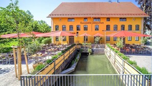 A yellow building with outdoor seating and a canal. - Hotel Kunstmühle (Mindelheim)