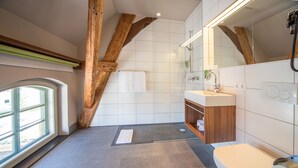 A modern bathroom with a wooden ceiling, a large mirror, a toilet, and a sink. - Hotel Kunstmühle (Mindelheim)