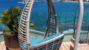 A wicker swing chair with a cushion, a potted plant, and a view of the sea and buildings in the background. - Spring Arona Gran Hotel & SPA - Adults Only (Arona)