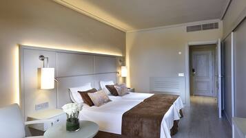 Una habitación de hotel con una cama grande, mesitas de noche, una pequeña mesa con un jarrón de flores y una puerta que da a otra habitación.