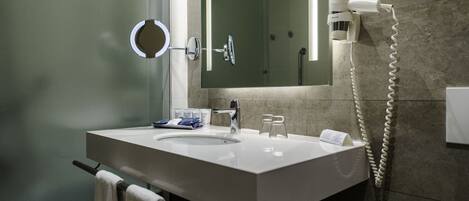 A modern bathroom with a double sink, a round mirror, a handheld showerhead, and a telephone.