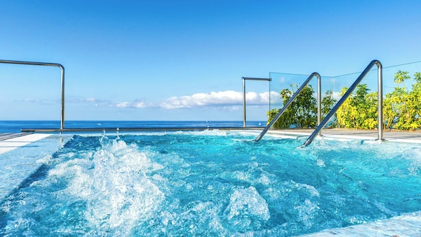 A clear blue pool with metal railings, surrounded by a tiled deck and palm trees, with a view of the ocean in the background. - Spring Arona Gran Hotel & SPA - Adults Only (Arona)
