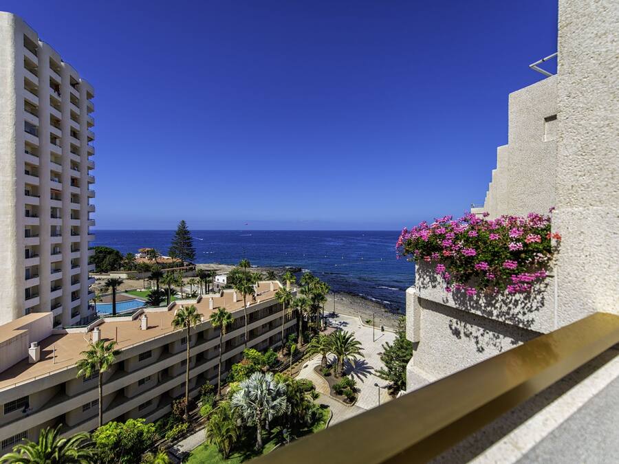Un hotel moderno con vistas al océano, piscina y una zona ajardinada con palmeras.