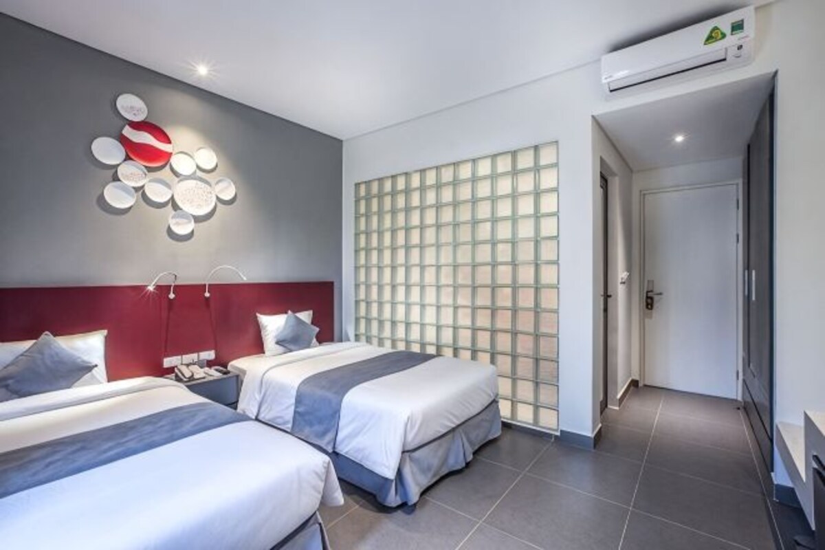 Habitación de hotel con dos camas, una pared de acento roja, un elemento decorativo en la pared y una puerta corredera que da a otra habitación.