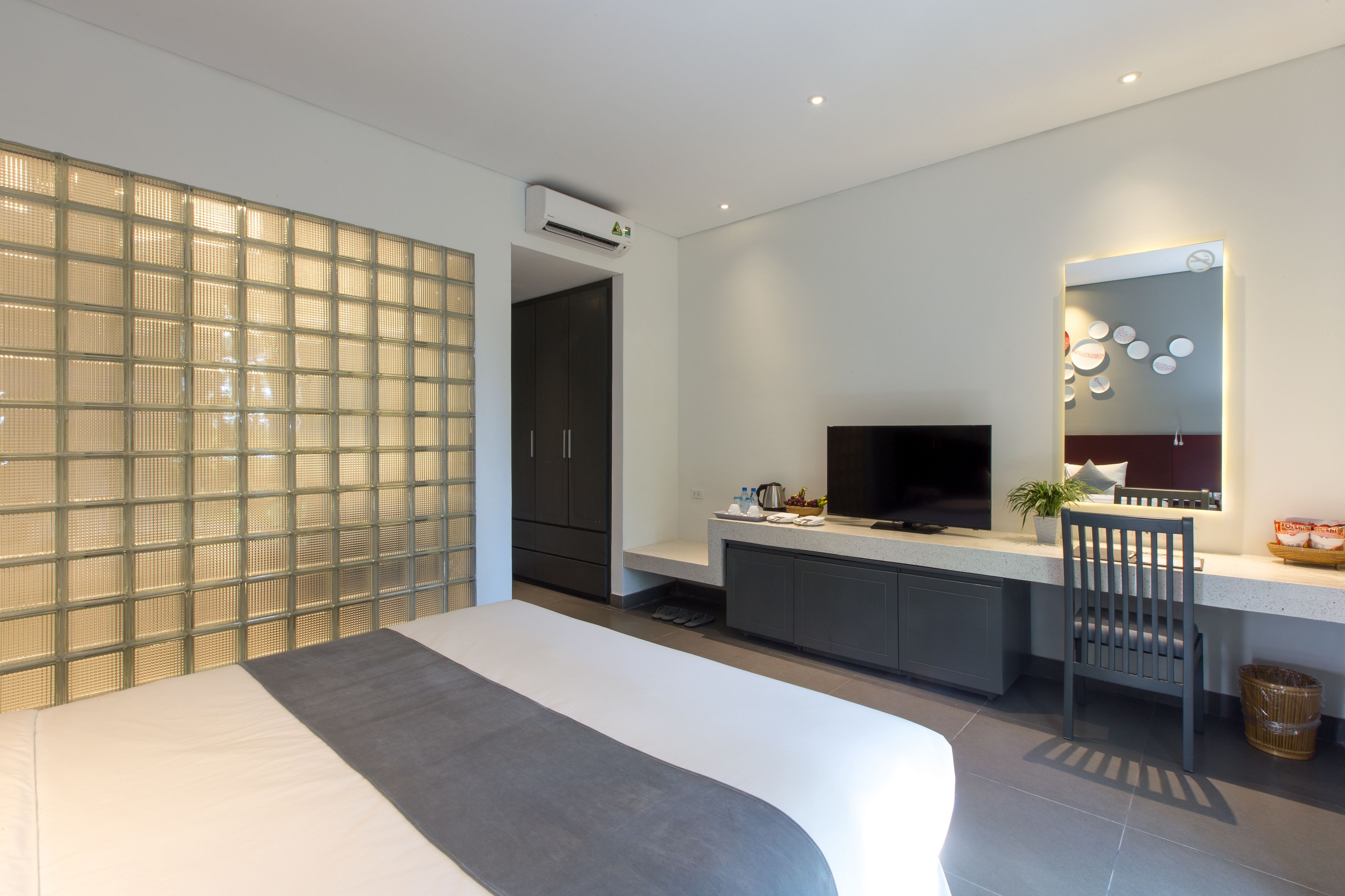 Una habitación de hotel moderna con una cama grande, un escritorio con computadora, televisor y una cocina equipada con microondas y tostadora.
