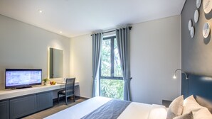 Une chambre d’hôtel moderne avec un grand lit, un téléviseur posé sur un bureau, une fenêtre avec des rideaux et un miroir fixé au mur.