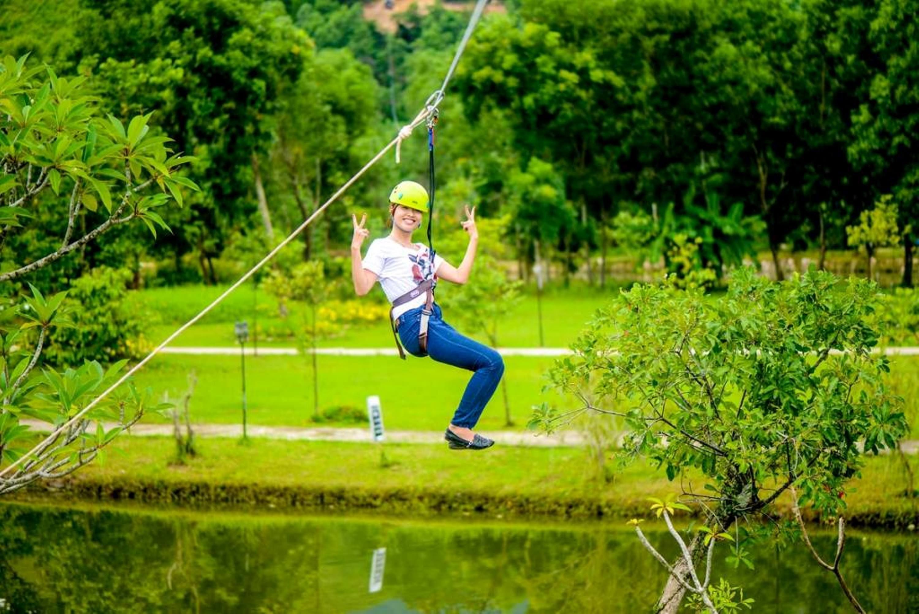 Eine Person zipline über ein Gewässer, im Hintergrund grüne Landschaft.