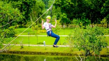 Eine Person zipline über ein Gewässer, im Hintergrund grüne Landschaft.