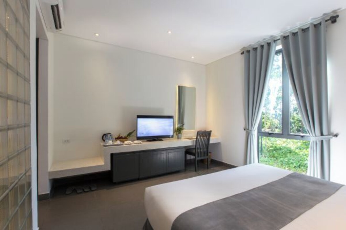 Una habitación de hotel moderna con una cama grande, un escritorio con computadora, un televisor y una ventana con cortinas.