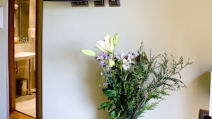 Una habitación con una televisión montada en la pared, un florero con flores sobre una mesa y un acceso a un baño.