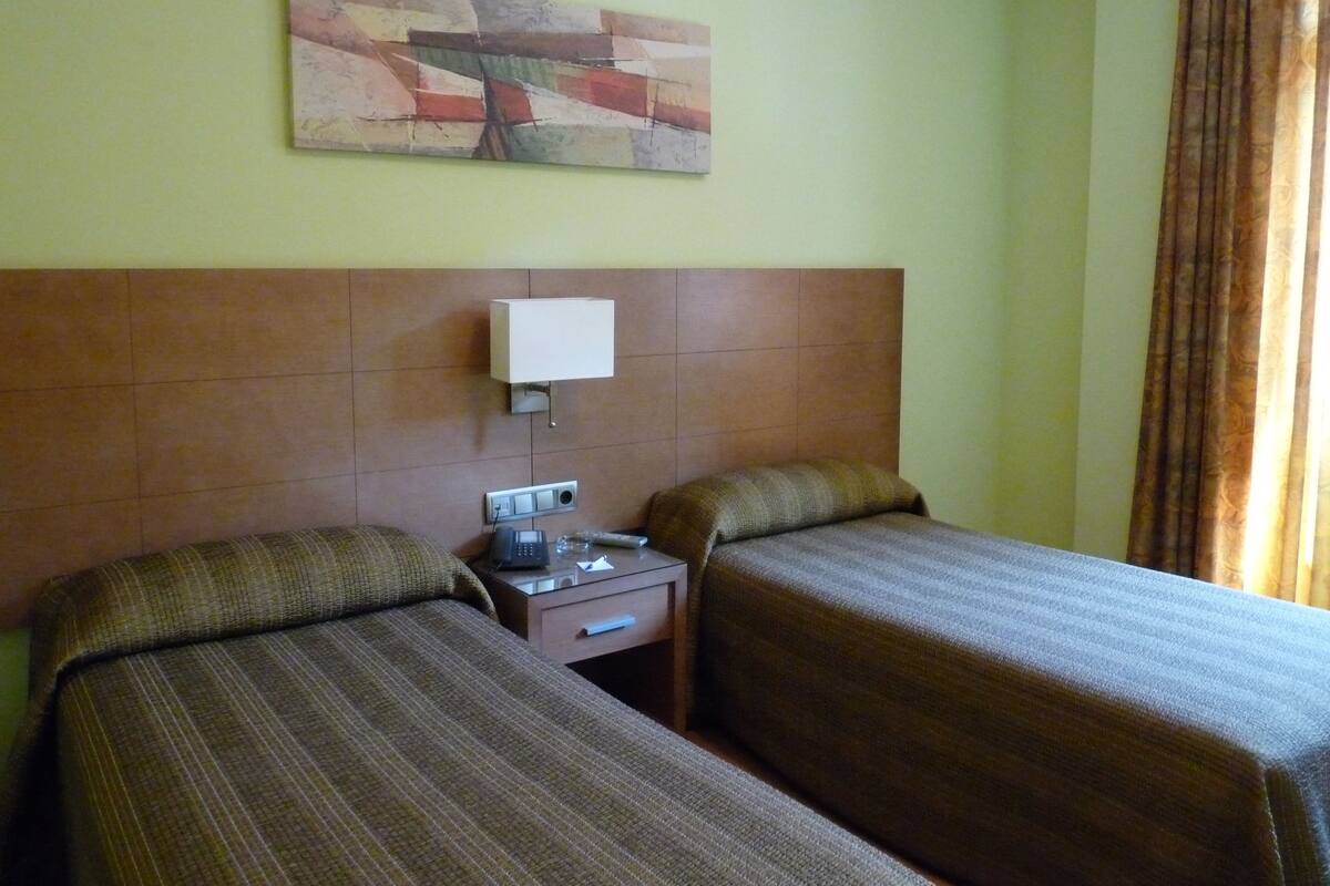 A hotel room with two beds, a nightstand, a lamp, and a painting on the wall.