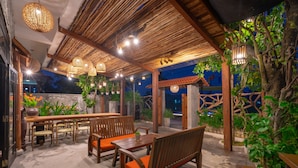 An outdoor patio area with wooden furniture, hanging lights, and potted plants. - Cat Tuong Boutique Villas (Da Nang)